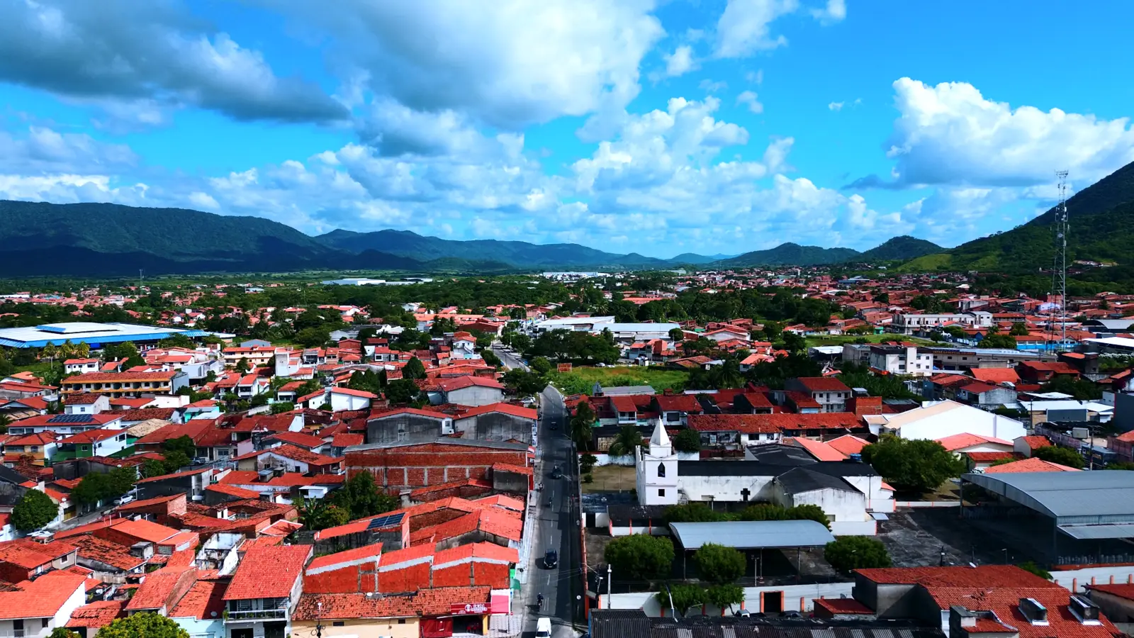 Panorama aéreo de Maranguape sob céu azul com nuvens, telhados cerâmicos e a serra ao fundo