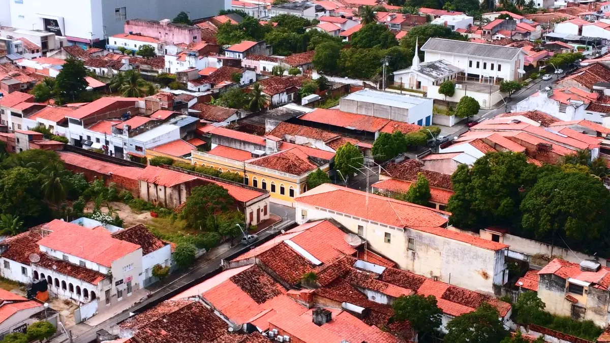 Vista aérea de ruas do centro com casarões de telhados cerâmicos e uma fachada amarela em destaque